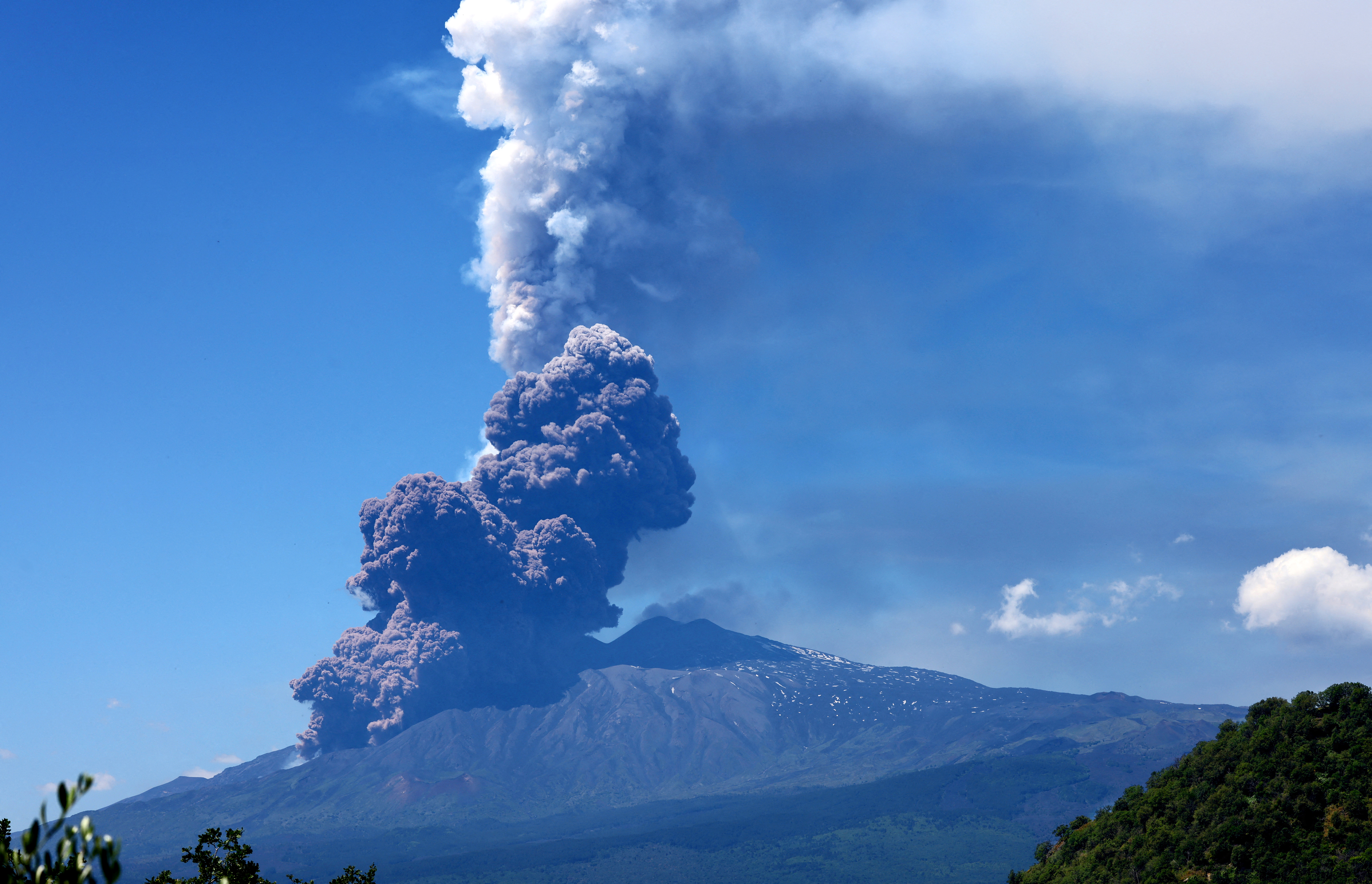 Erupting Mount Etna with a plume rising against clear skies.