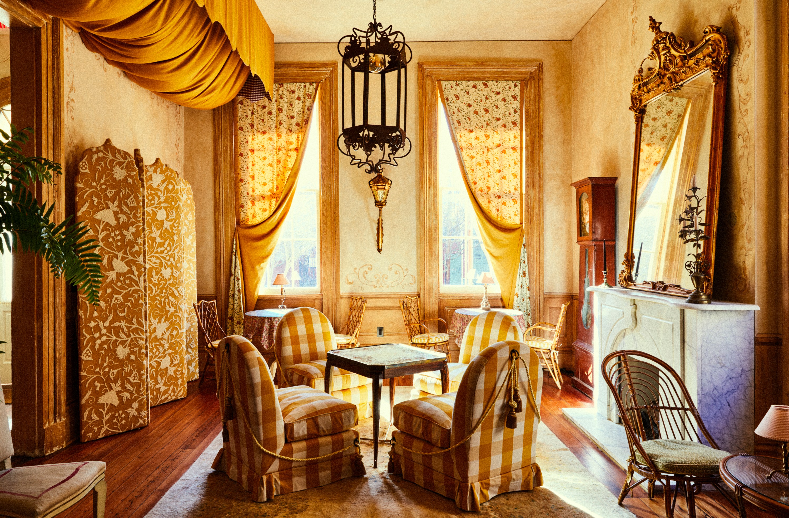 Interior view of a room with yellow and white checkered chairs, a patterned room divider, and a marble fireplace.
