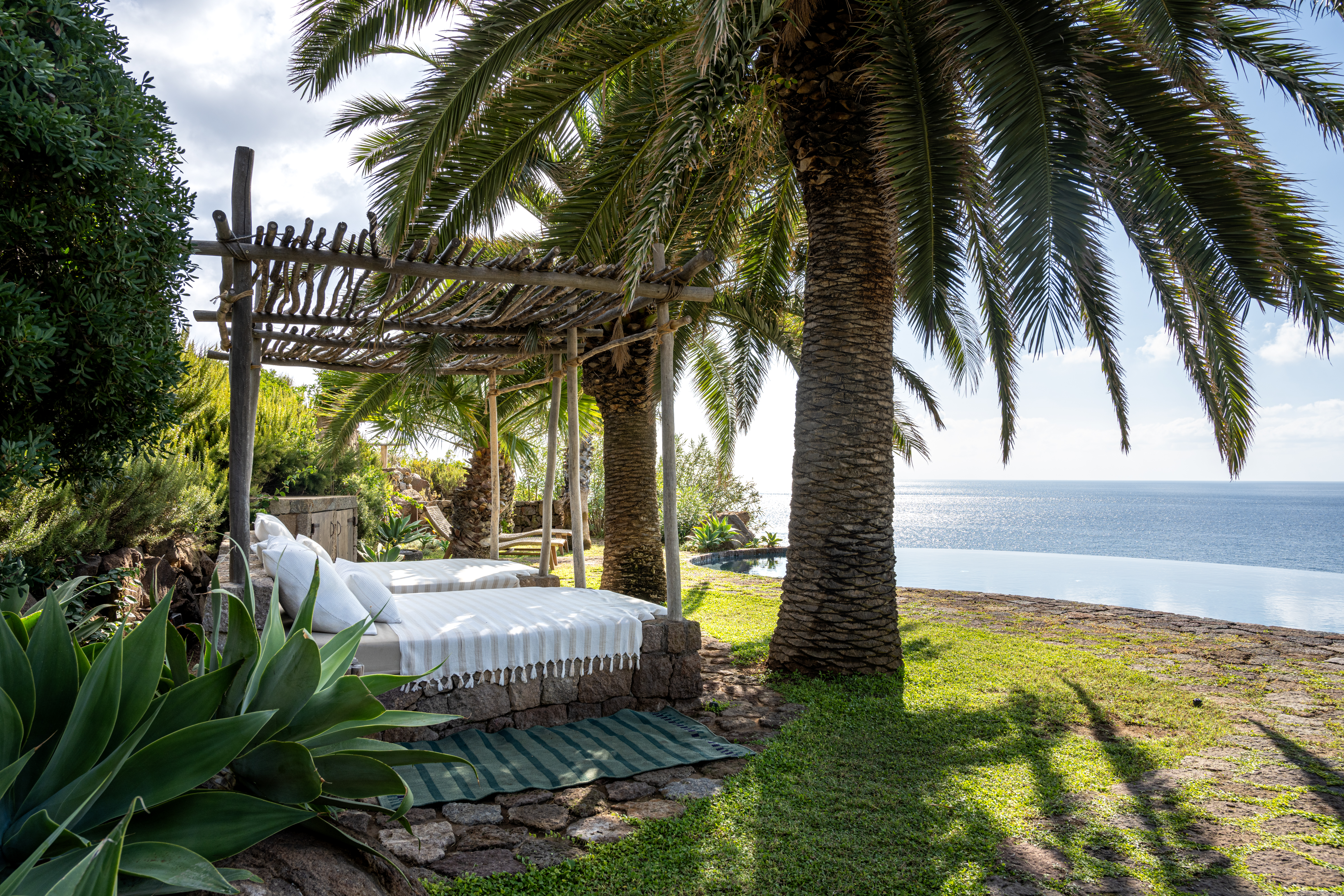 A bed under a palm tree by the sea at Antika, Panarea, Aeolian Islands, one of the best villas in Italy with a pool