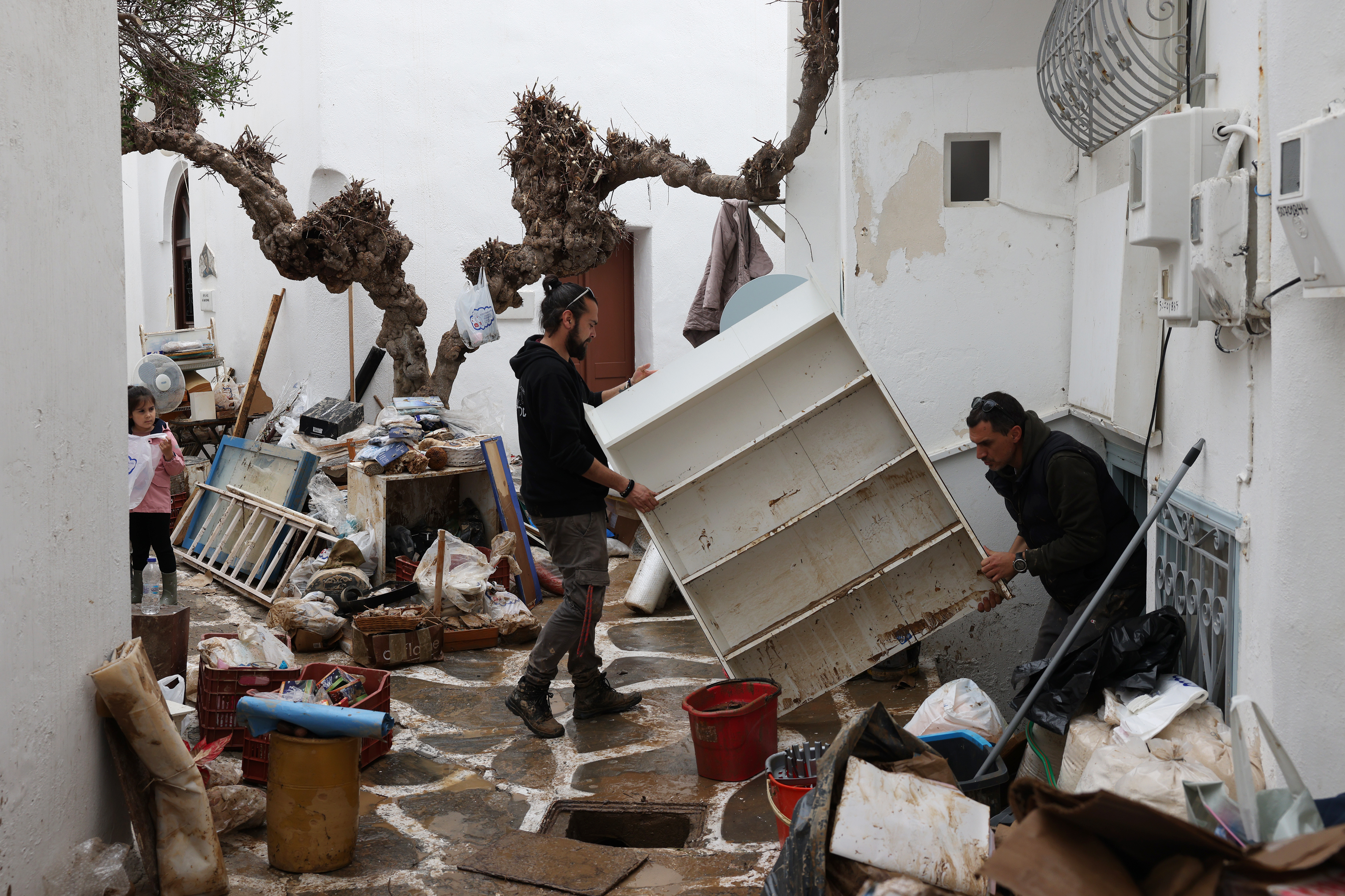 People removing mud-covered furniture from a flooded building in Paros, Greece.