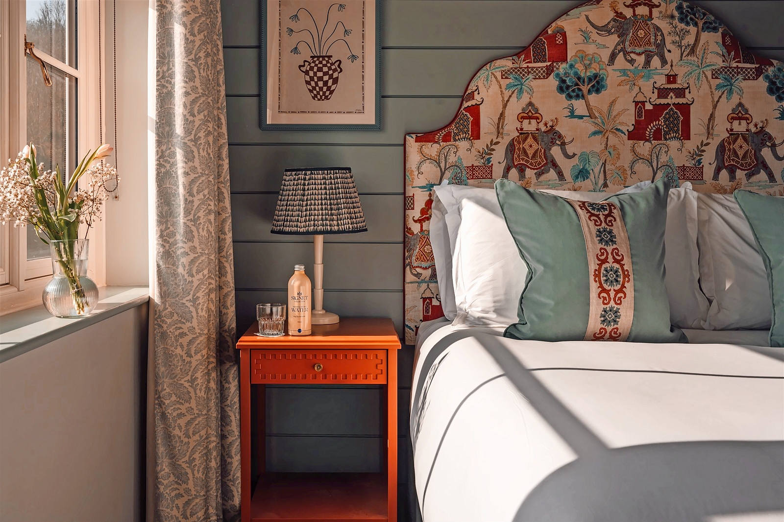 Alfriston hotel room detail: bed with patterned headboard, bedside table with water bottle and lamp.