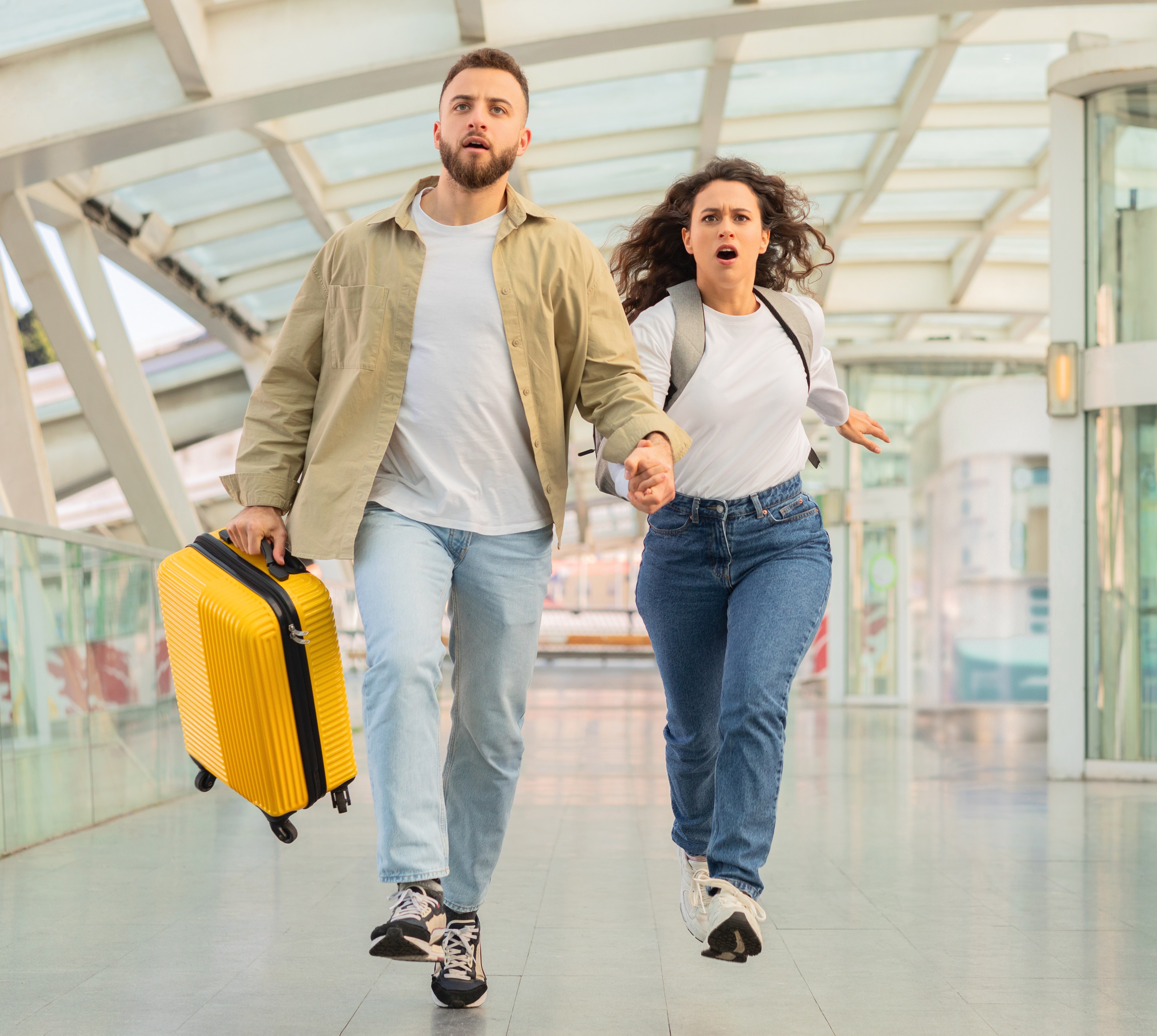 A young couple rushes through an airport terminal with luggage.