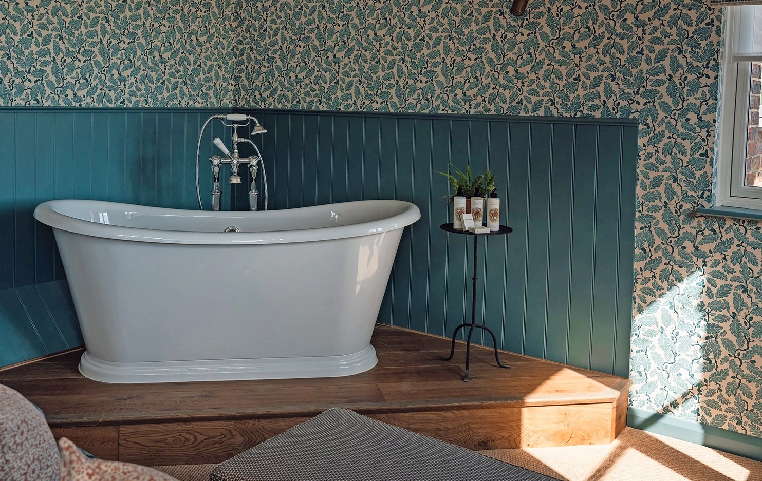 Freestanding bathtub in a corner of a teal-walled bathroom.